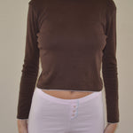 Person wearing a brown long-sleeve top and pink shorts on a plain background