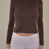 Person wearing a brown long-sleeve top and pink shorts on a plain background