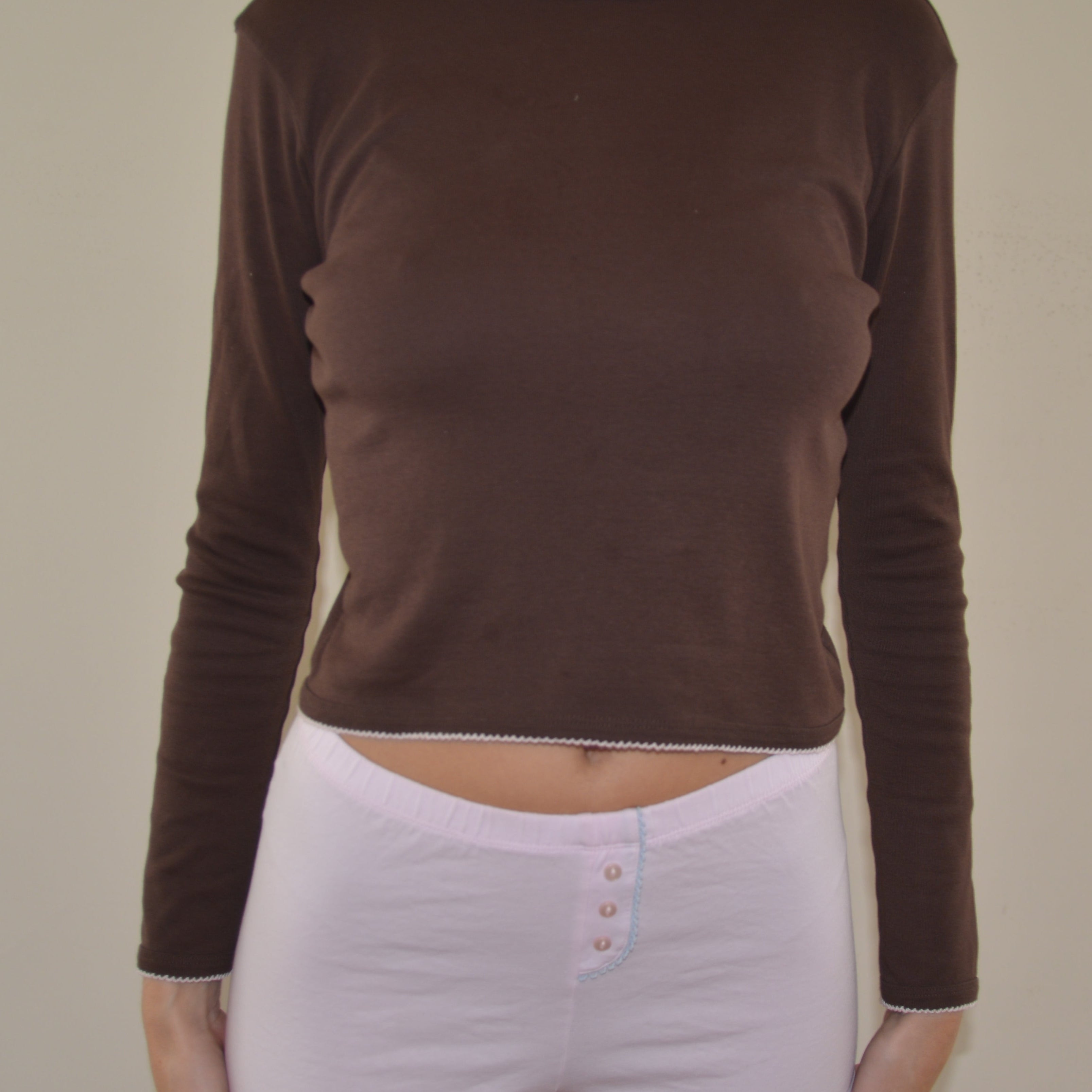 Person wearing a brown long-sleeve top and pink shorts on a plain background